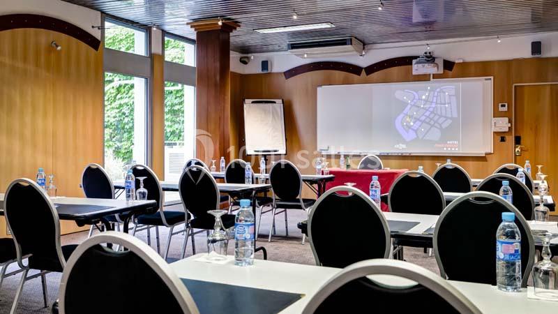 Salle de réunion équipée de tables, chaises, tableau blanc, écran de projection et bouteilles d'eau sur les tables.