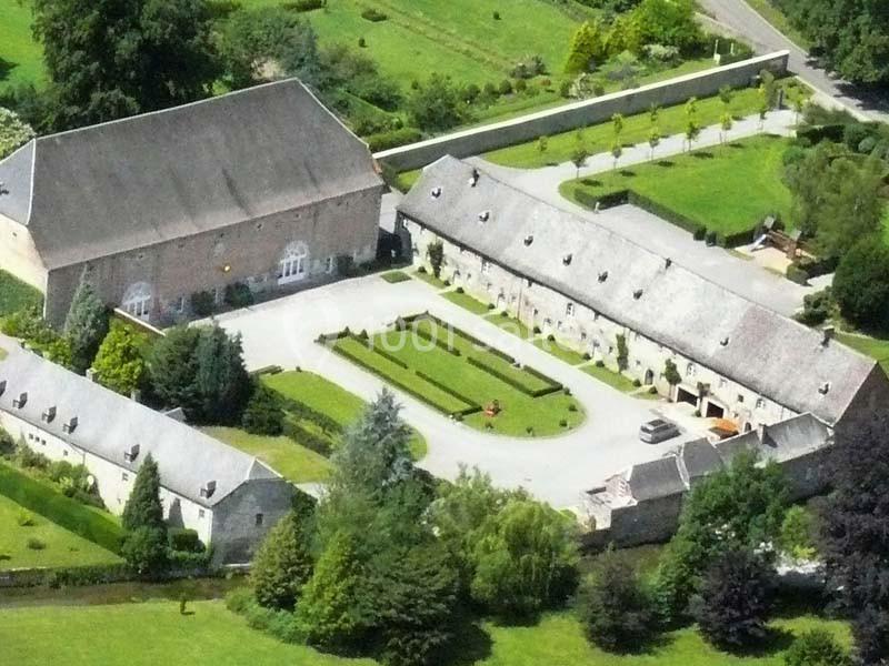 Vue aérienne d'un domaine avec bâtiments en pierre, cour centrale, jardins aménagés et espaces verts environnants.