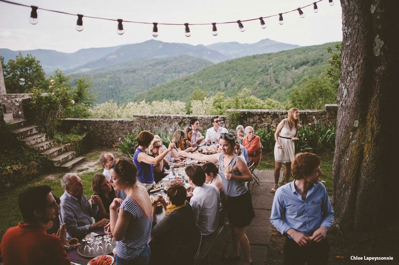 Un groupe de personnes partage un repas en plein air sur une terrasse avec vue sur des montagnes verdoyantes.