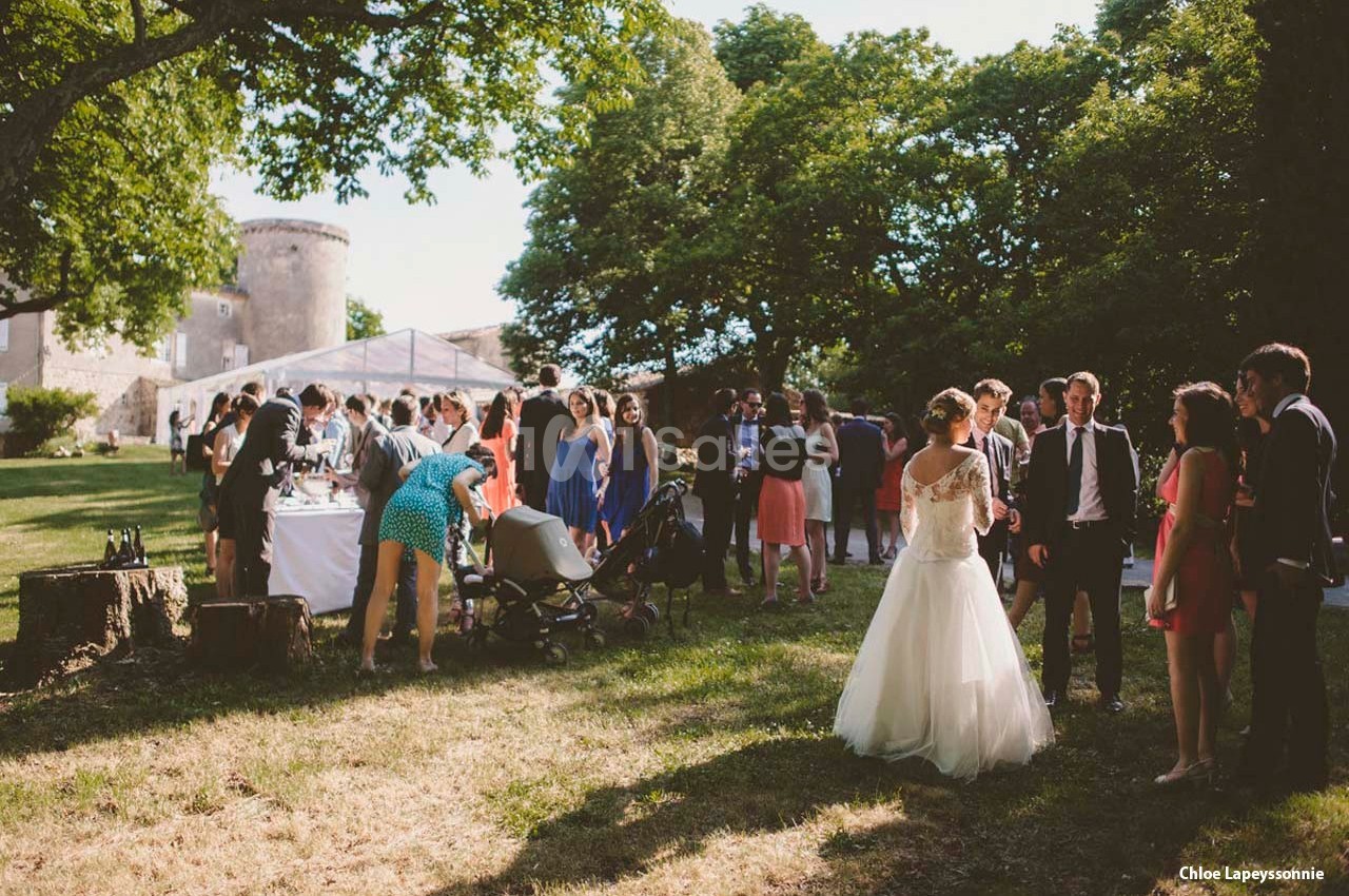 Groupe de personnes rassemblées en extérieur lors d'une réception, avec une mariée en robe blanche au premier plan.