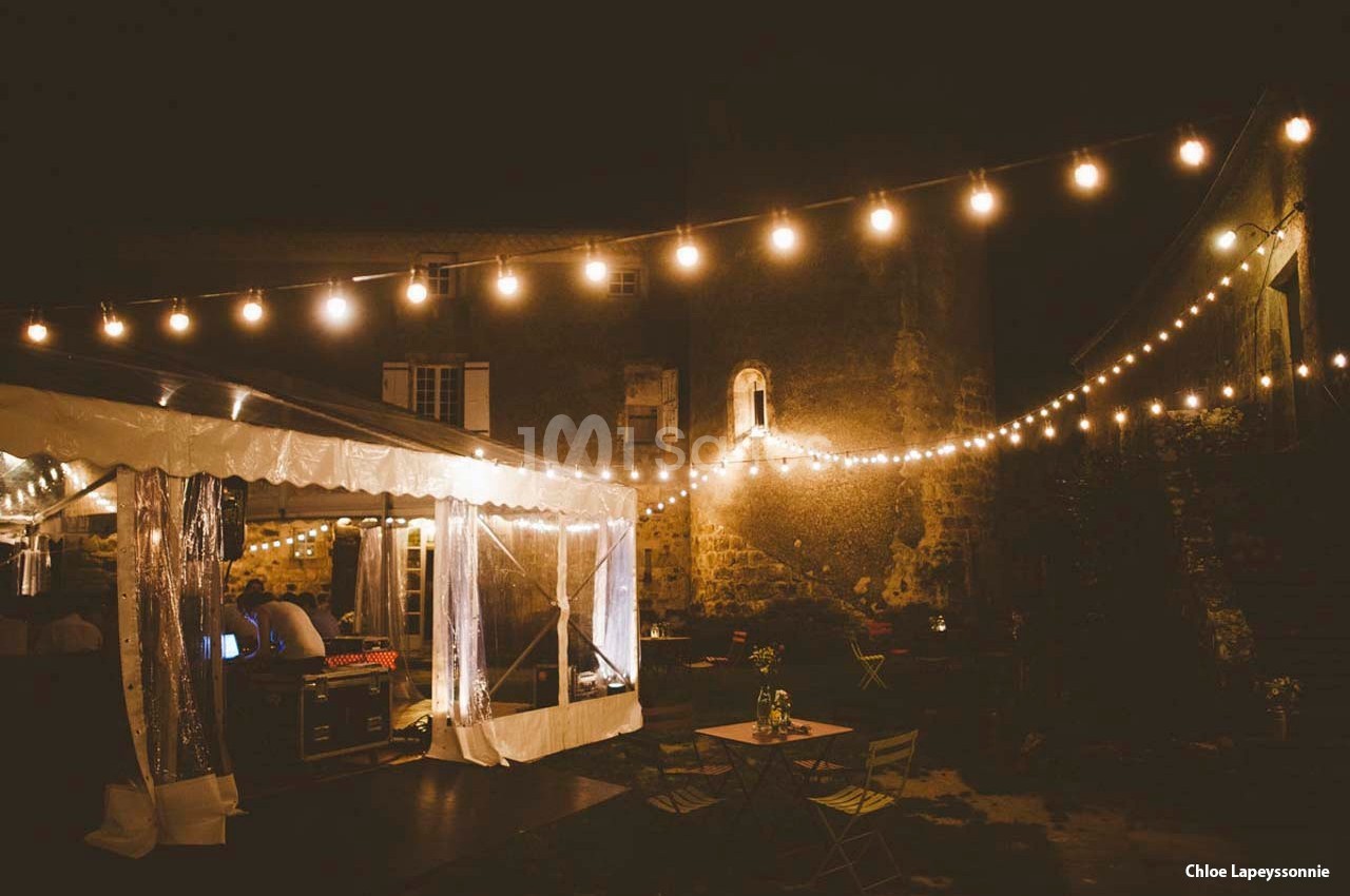 Guirlandes lumineuses suspendues éclairant une cour extérieure avec des tables et une tente transparente, de nuit.