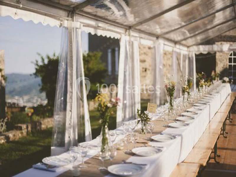 Table dressée sous une tente transparente, décorée de fleurs et de vaisselle, dans un cadre extérieur ensoleillé.