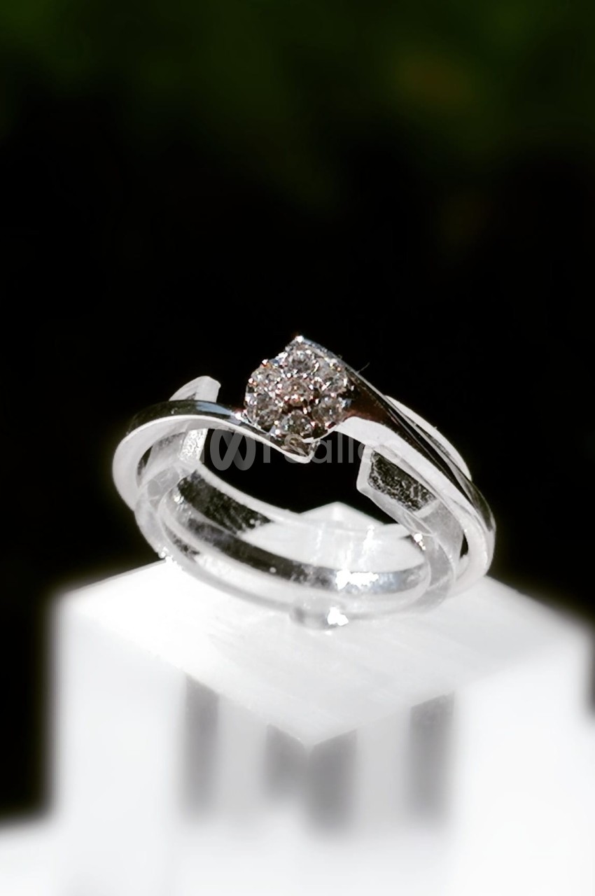 Bague en argent ornée d'un diamant central, posée sur un support blanc avec un arrière-plan sombre.