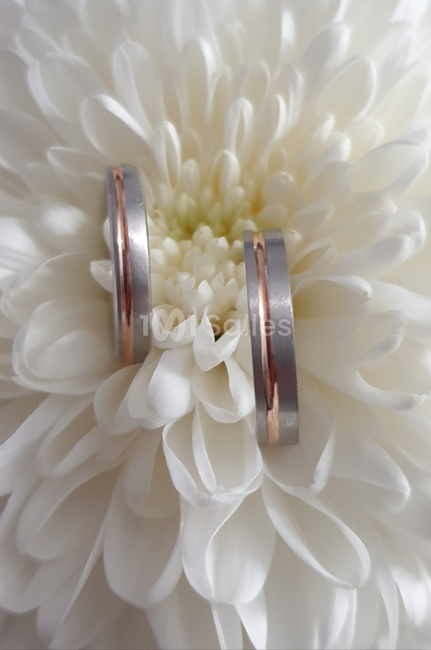 Deux alliances bicolores en argent et or rose posées sur une fleur blanche en gros plan.