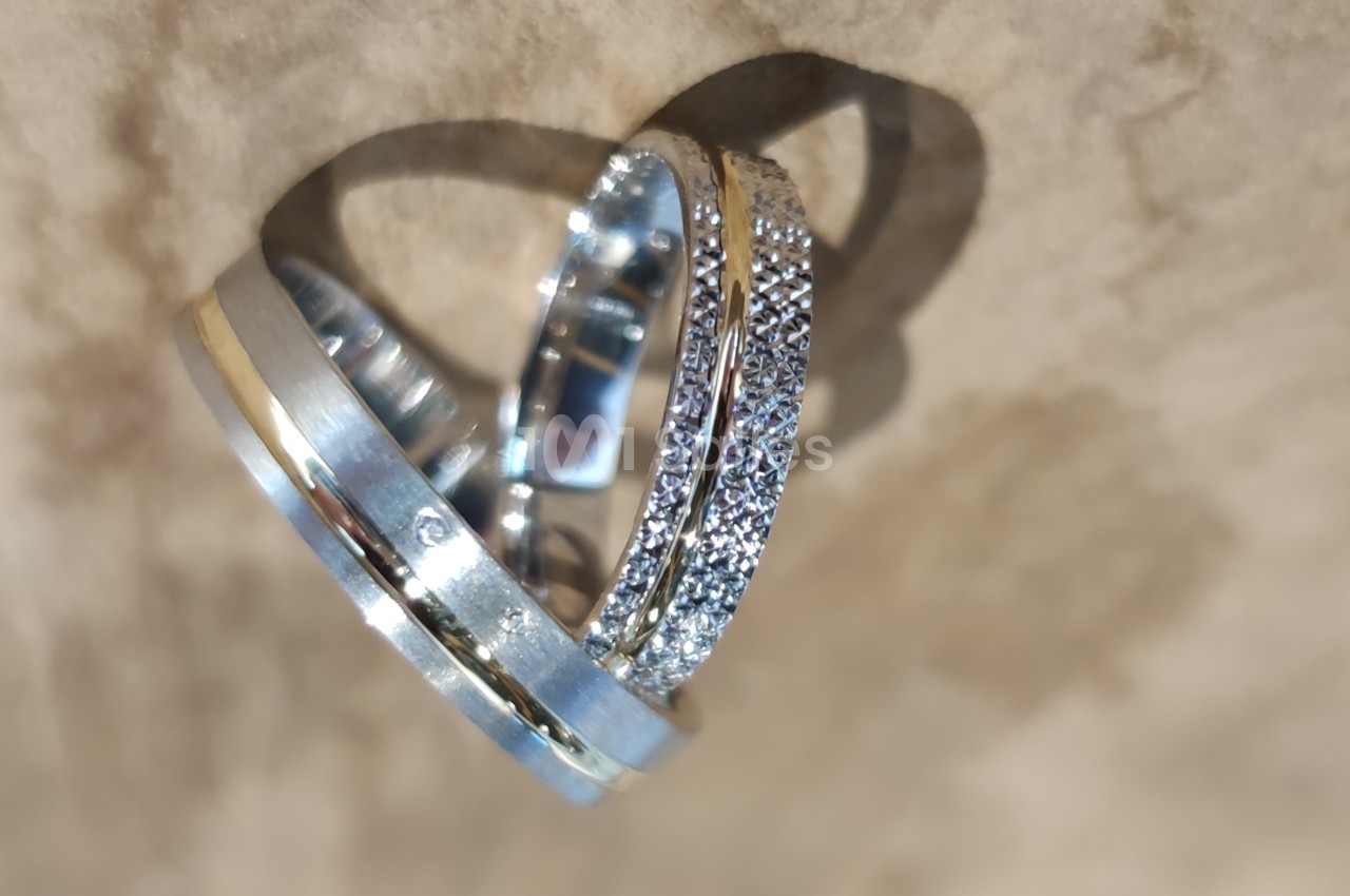 Deux alliances en métal argenté et doré, l'une ornée de petits diamants, posées sur une surface beige.
