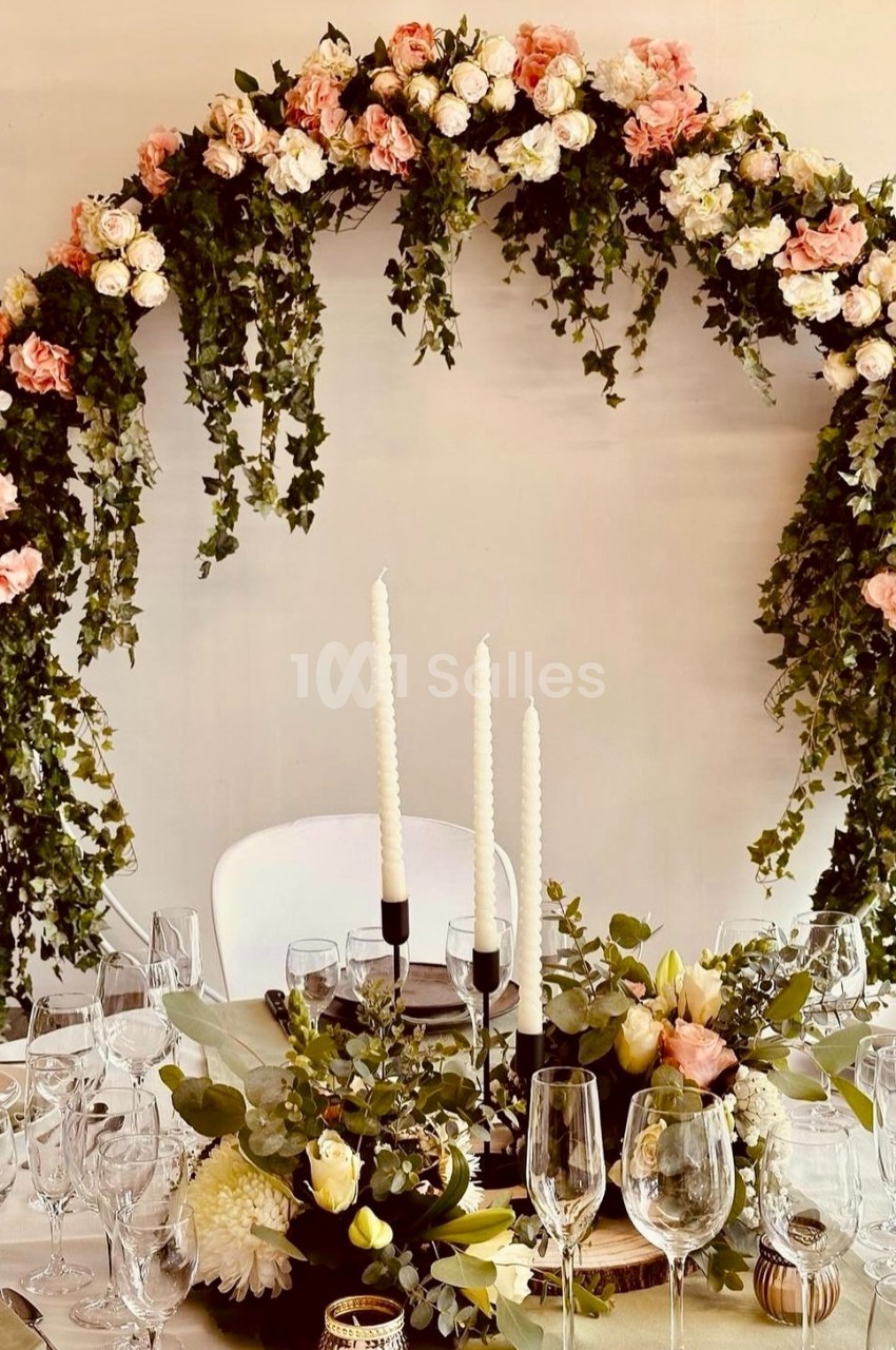 Arche florale ornée de roses et de feuillage au-dessus d'une table décorée avec des bougies et des arrangements floraux.
