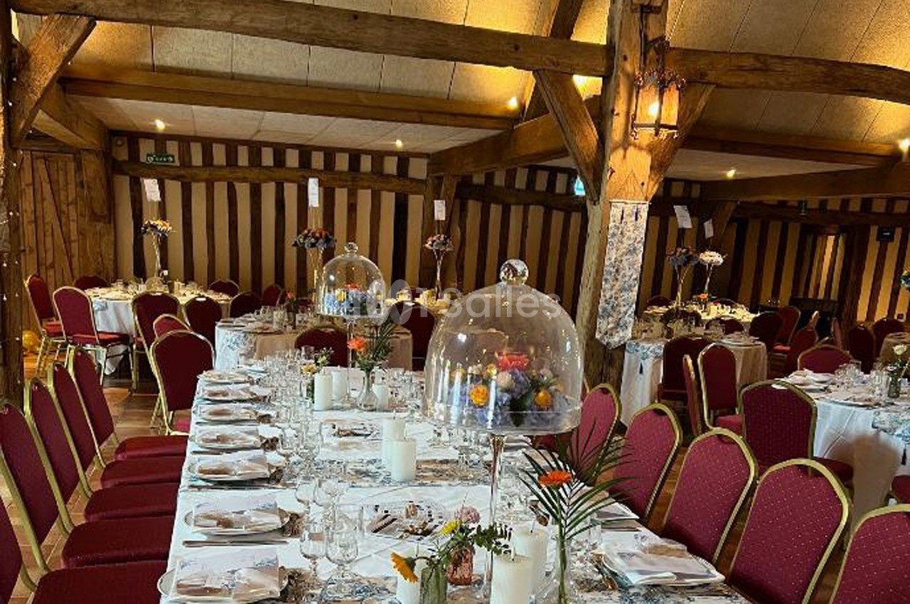 Salle de réception décorée avec des tables dressées, chaises rouges et centres de table sous cloches en verre.