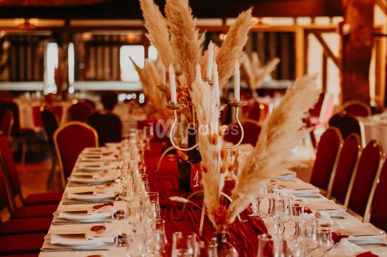 Table dressée avec nappes blanches, décorations de pampas et chandeliers dorés dans une salle aux tons chaleureux.
