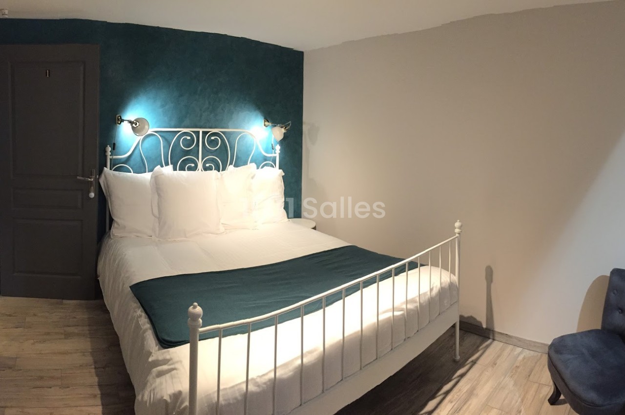 Lit double avec tête de lit en métal blanc, draps blancs, plaid vert, mur bleu et éclairage mural dans une chambre.