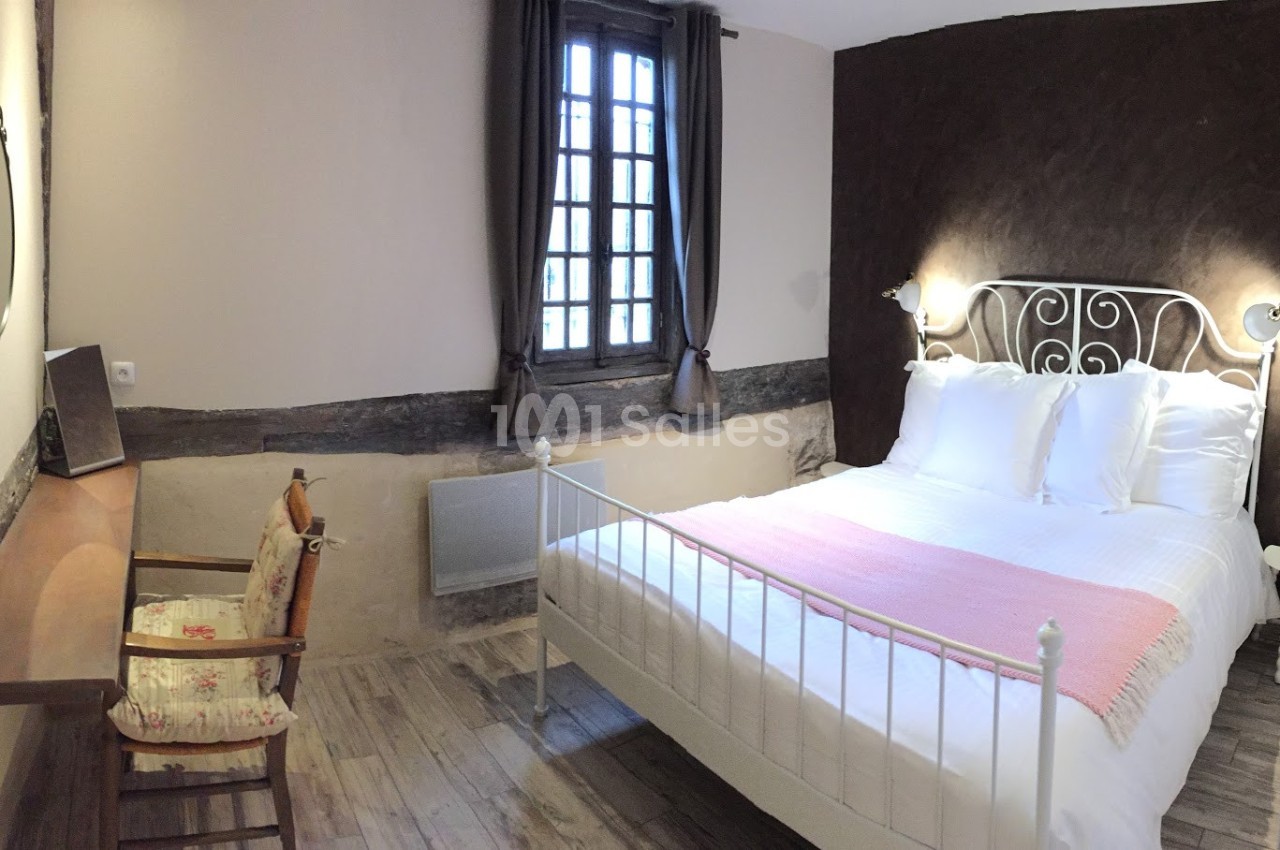 Chambre avec lit double, mur en bois apparent, bureau, chaise et fenêtre avec rideaux sombres.