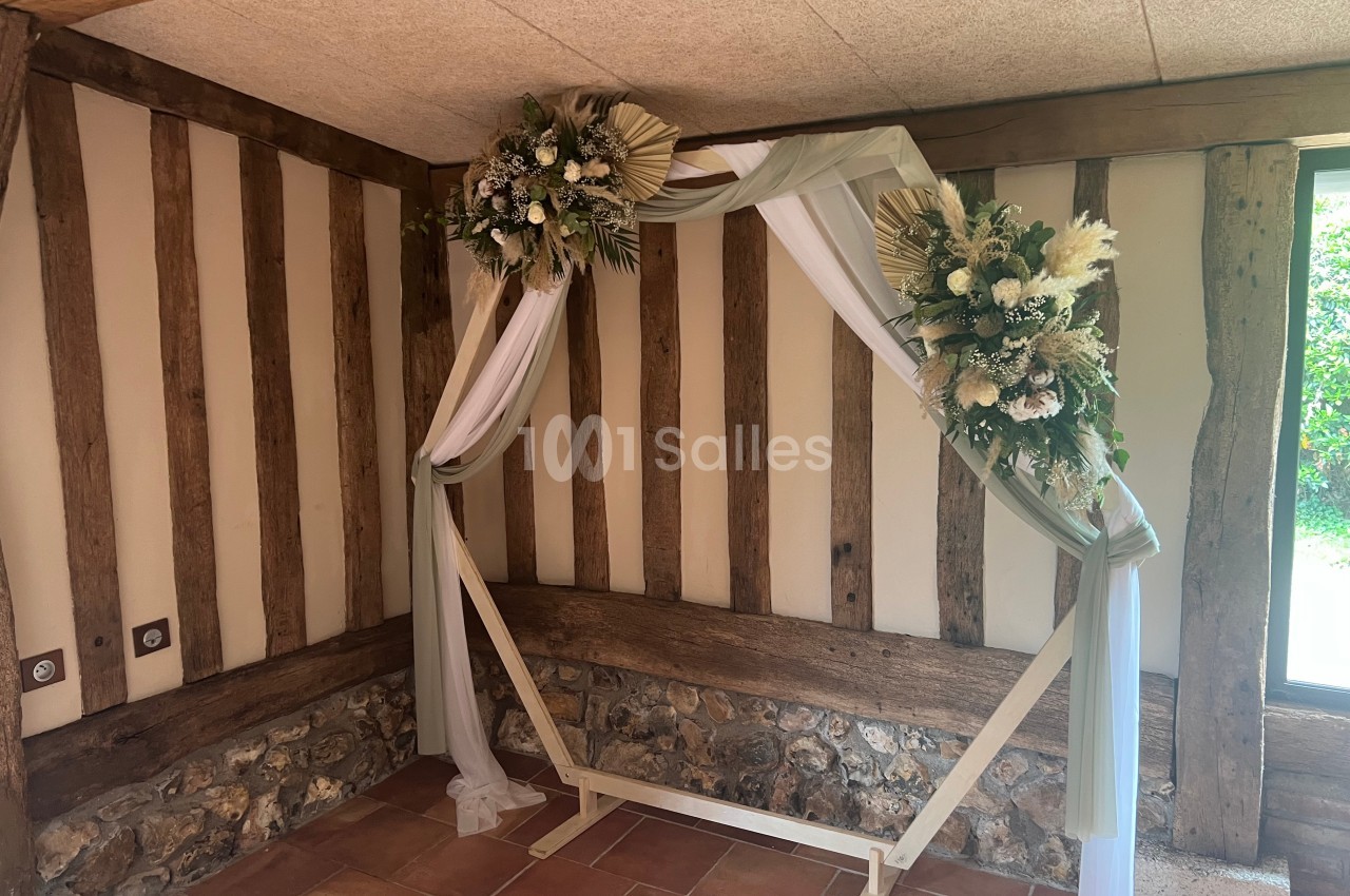 Arche décorative en bois ornée de fleurs séchées et de voilages blancs dans une pièce aux murs en colombages.