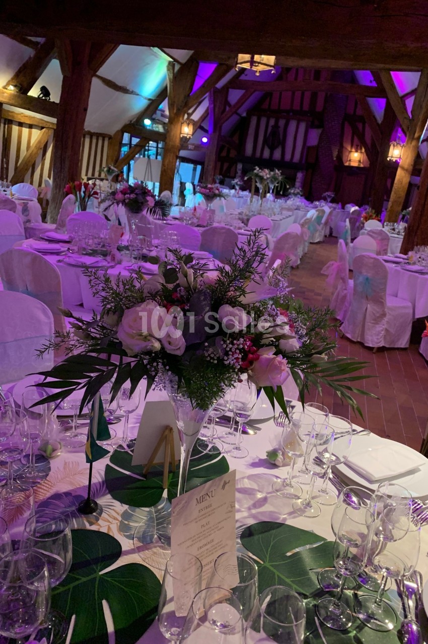 Salle de réception décorée avec des tables dressées, nappes blanches, bouquets floraux et éclairage tamisé.