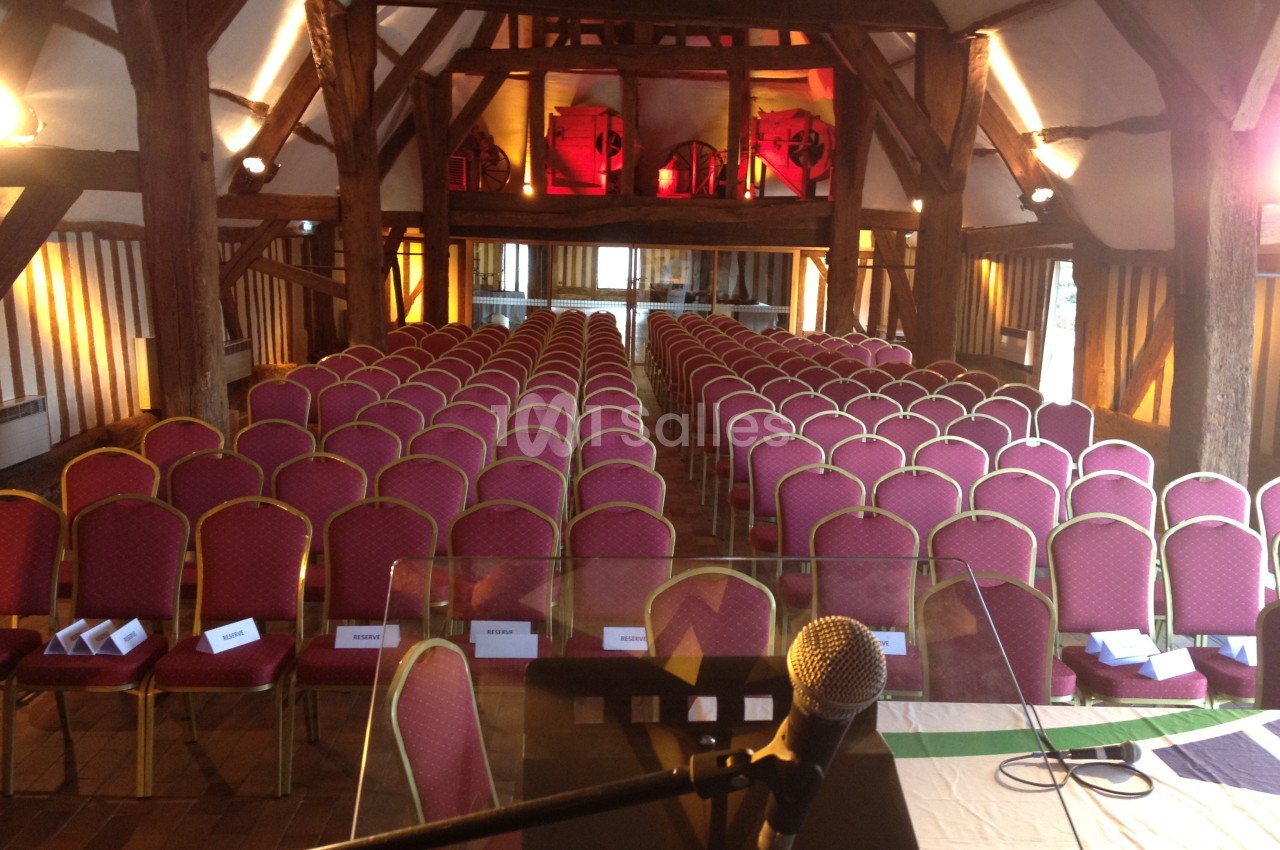 Salle de conférence avec des rangées de chaises rouges alignées, vue depuis un pupitre équipé d’un microphone.