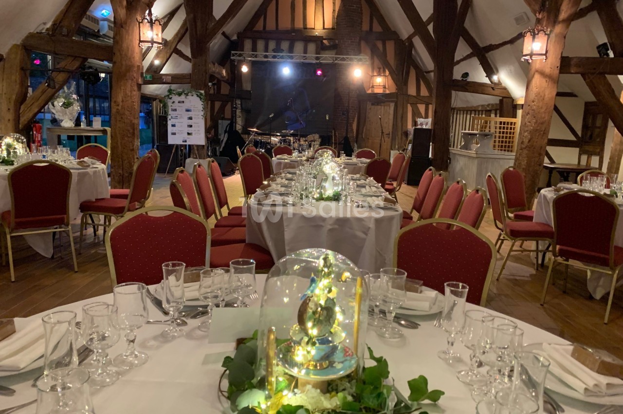 Salle de réception décorée avec des tables dressées, des chaises rouges et des centres de table lumineux sous cloche.