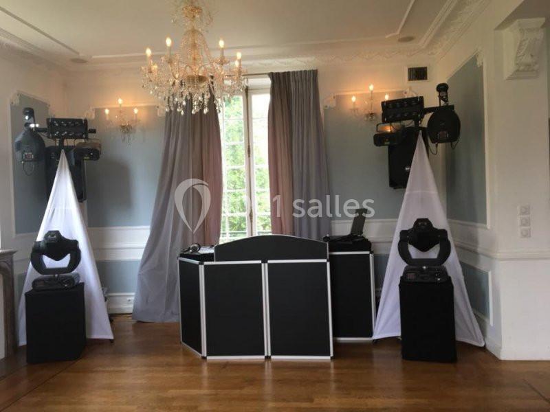 Installation de matériel de sonorisation et d'éclairage dans une salle avec parquet, rideaux et lustre.