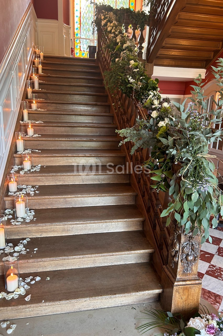 Escalier en bois décoré de bougies, pétales de fleurs blanches et guirlandes de feuillage, dans un intérieur lumineux.
