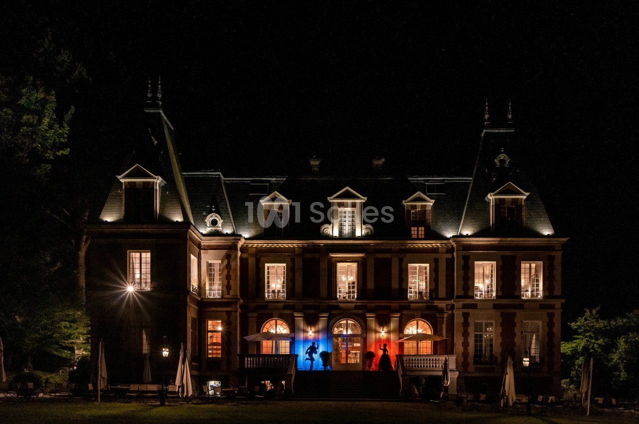 Façade d'un château illuminé de nuit, avec des lumières aux couleurs bleu, blanc et rouge.