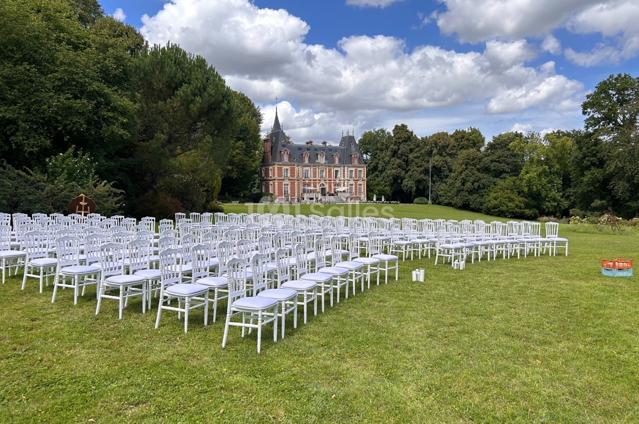 Chaises blanches alignées en extérieur sur une pelouse devant un château sous un ciel partiellement nuageux.