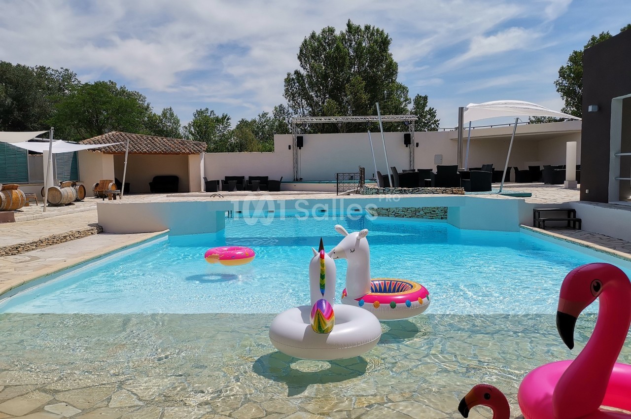 Piscine extérieure avec des bouées colorées en forme d'animaux, entourée de chaises et d'arbres sous un ciel dégagé.