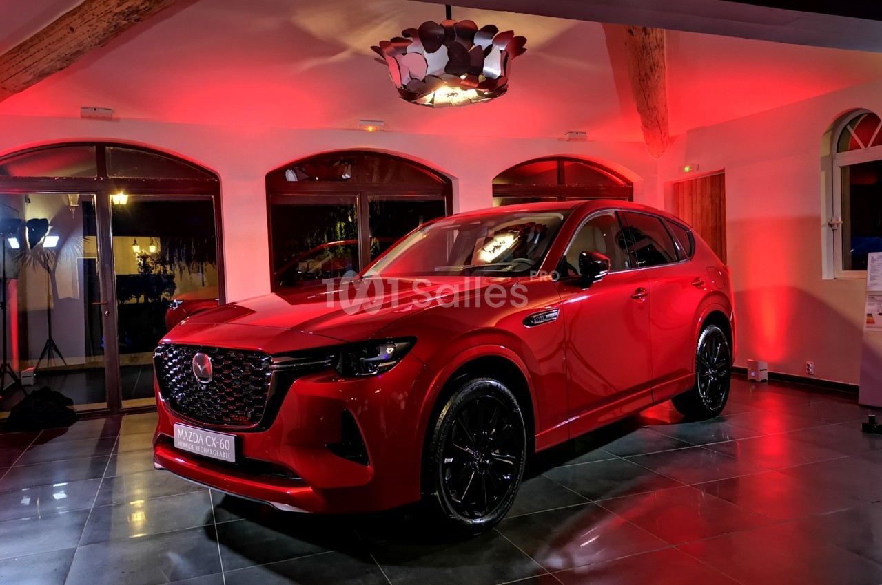 SUV rouge exposé dans une salle éclairée par des lumières rouges, avec des fenêtres et des poutres en bois visibles en…