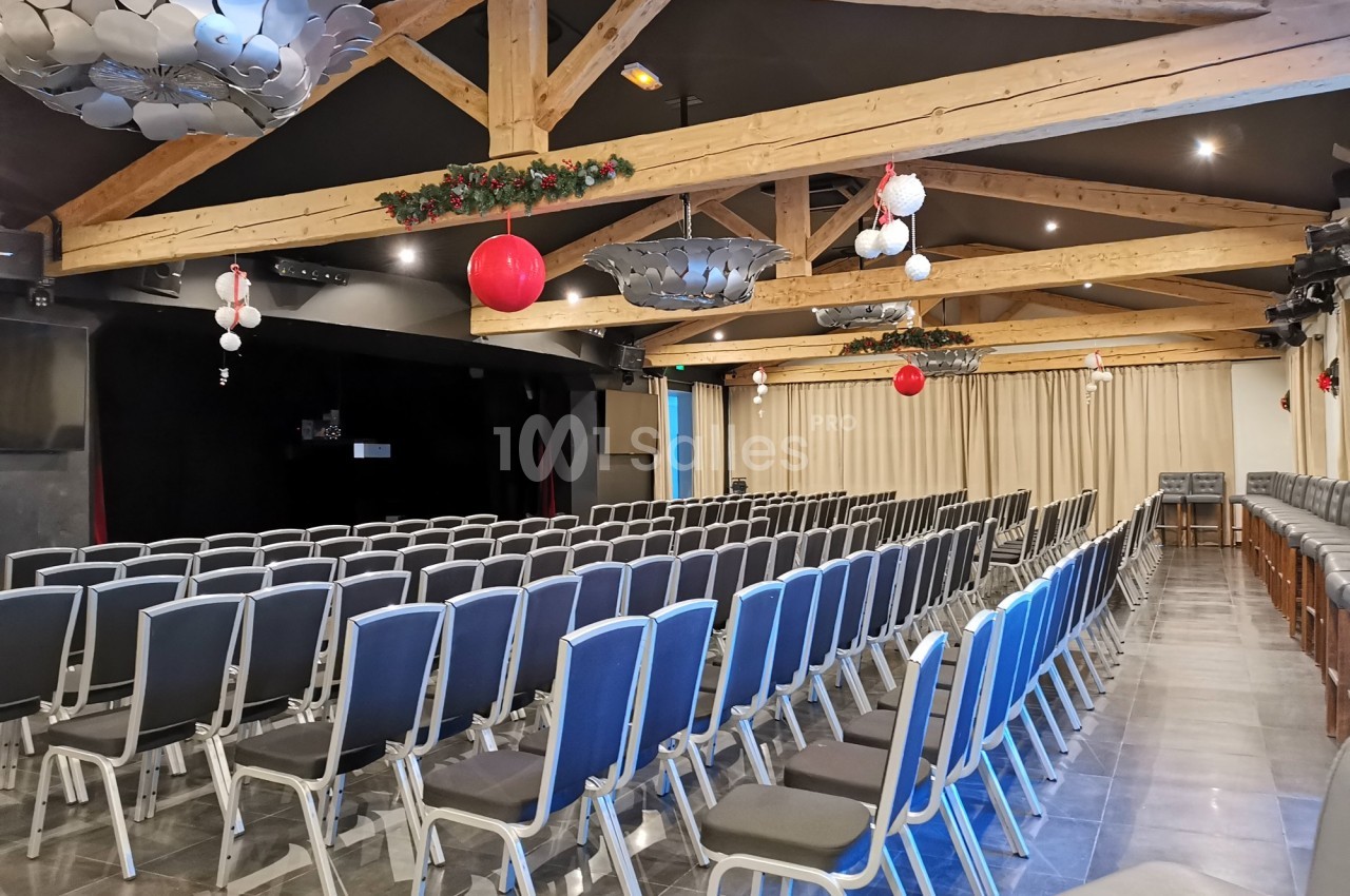 Salle de conférence avec rangées de chaises alignées, plafond en poutres apparentes et décorations suspendues.
