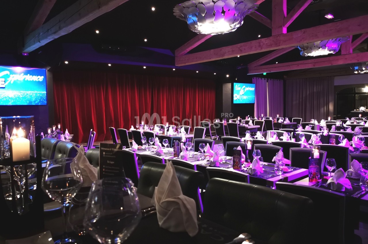 Salle de restaurant élégante avec tables dressées, nappes blanches, chandeliers et rideaux rouges en arrière-plan.