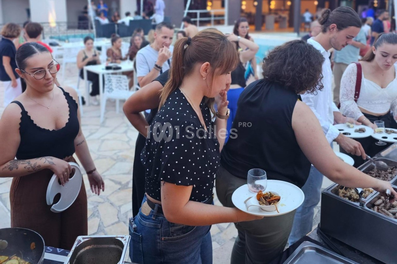 Des personnes font la queue pour se servir à un buffet en extérieur près d'une piscine.