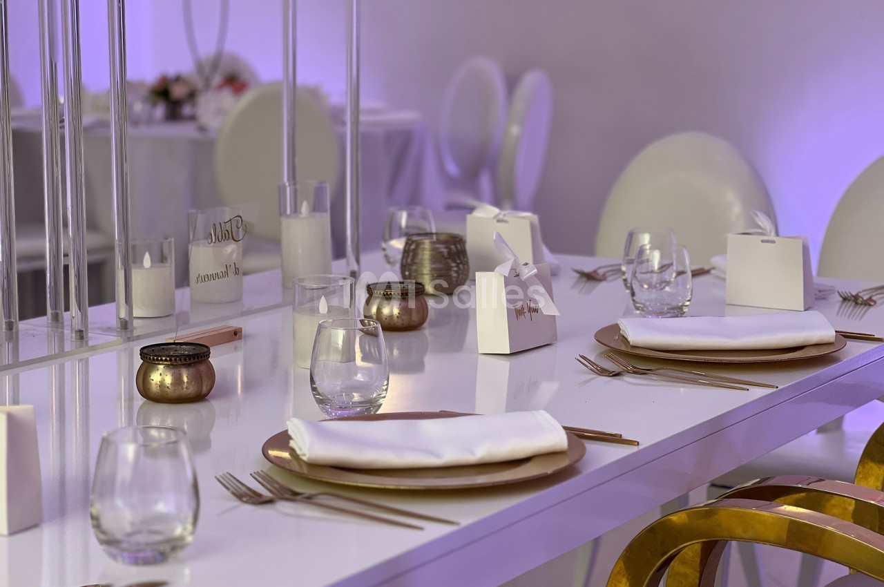 Table élégamment dressée avec assiettes dorées, serviettes blanches, verres et décorations minimalistes dans un cadre…