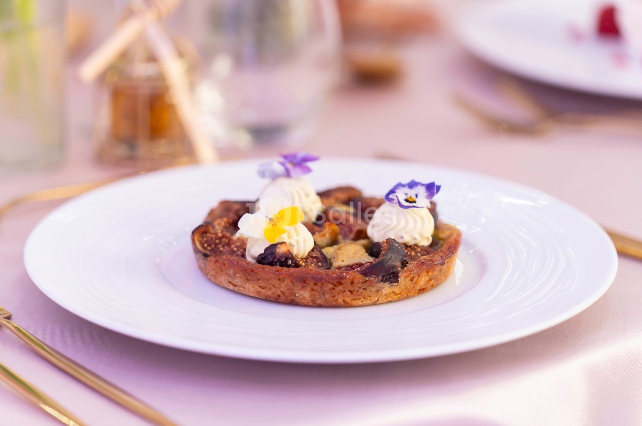 Tartelette garnie de figues, crème et fleurs comestibles, servie sur une assiette blanche dans un cadre élégant.