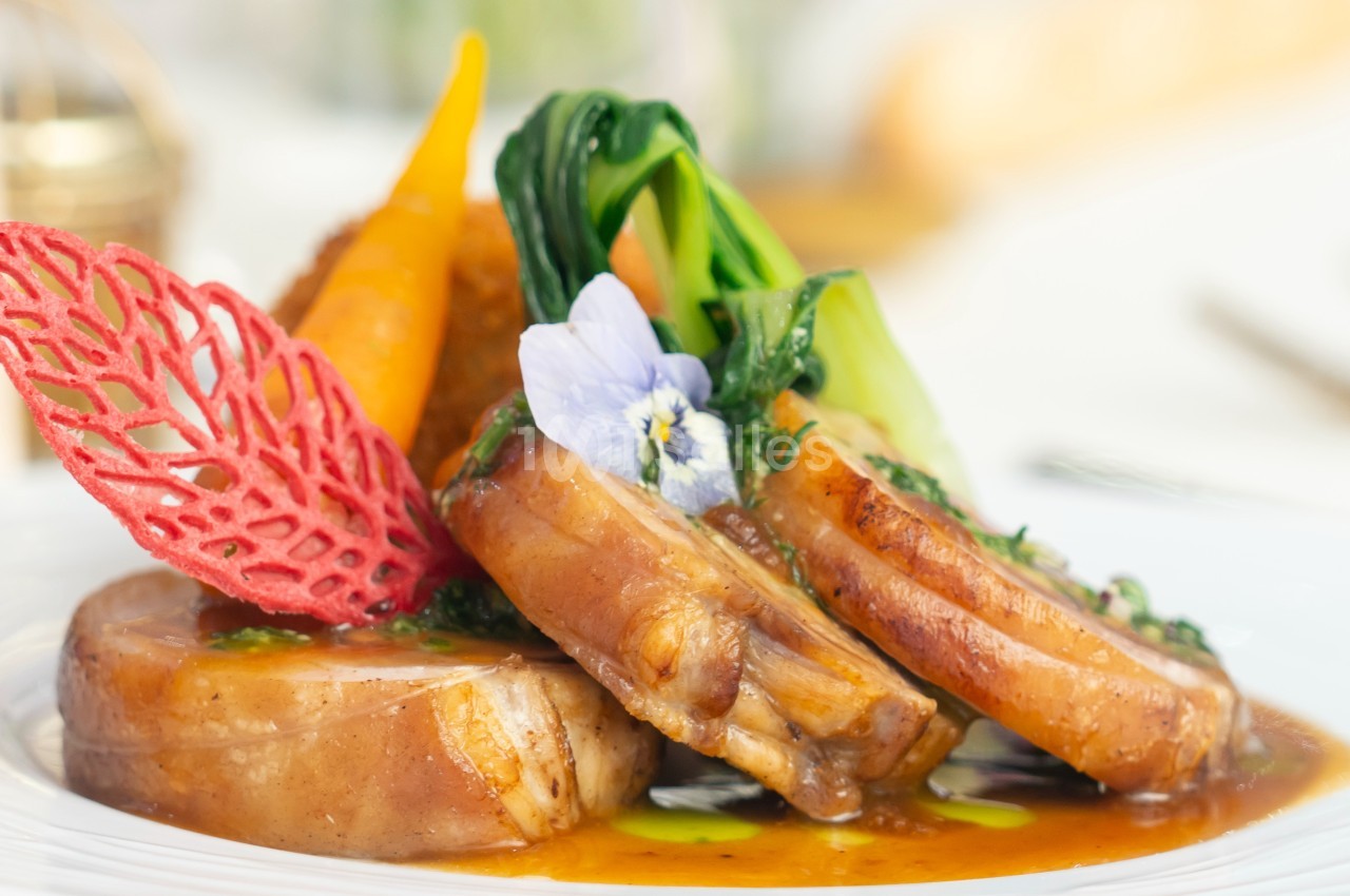 Plat gastronomique composé de viande, légumes colorés, sauce et décorations comestibles sur une assiette blanche.