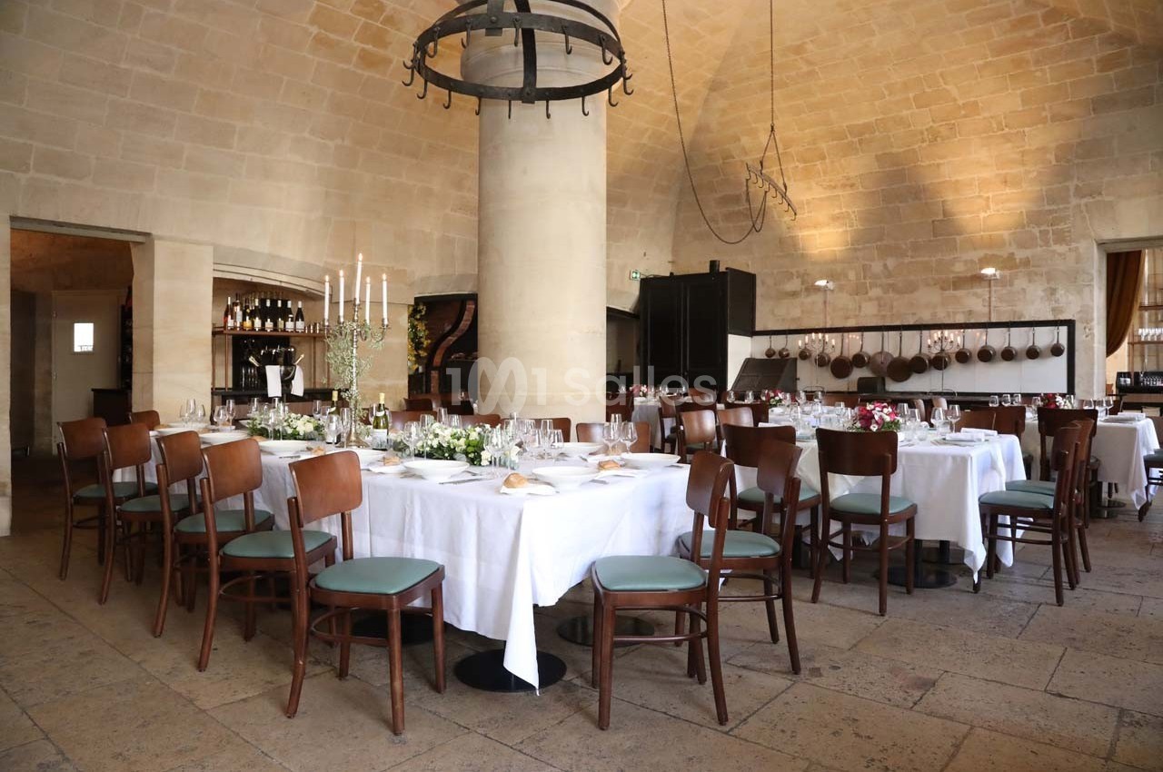 Salle de restaurant élégante avec tables dressées, nappes blanches, chaises en bois et murs en pierre apparente.