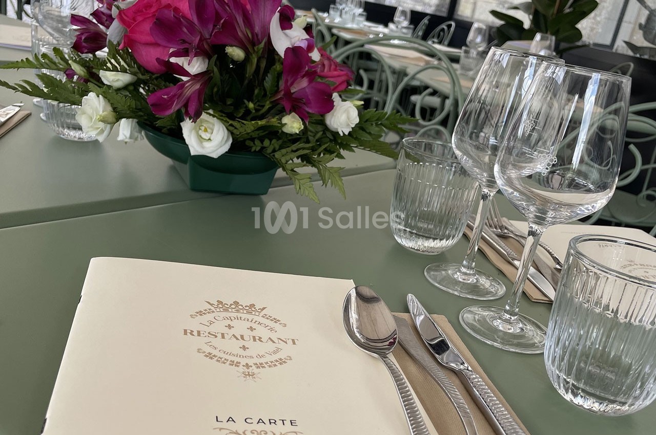 Menu posé sur une table dressée avec des couverts, verres et un bouquet de fleurs en arrière-plan.