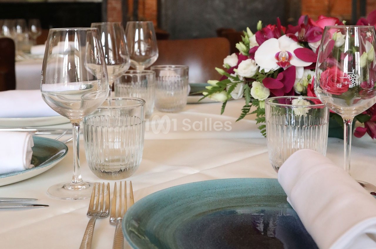 Table élégamment dressée avec assiettes, verres, couverts et centre de table floral dans un décor chaleureux.