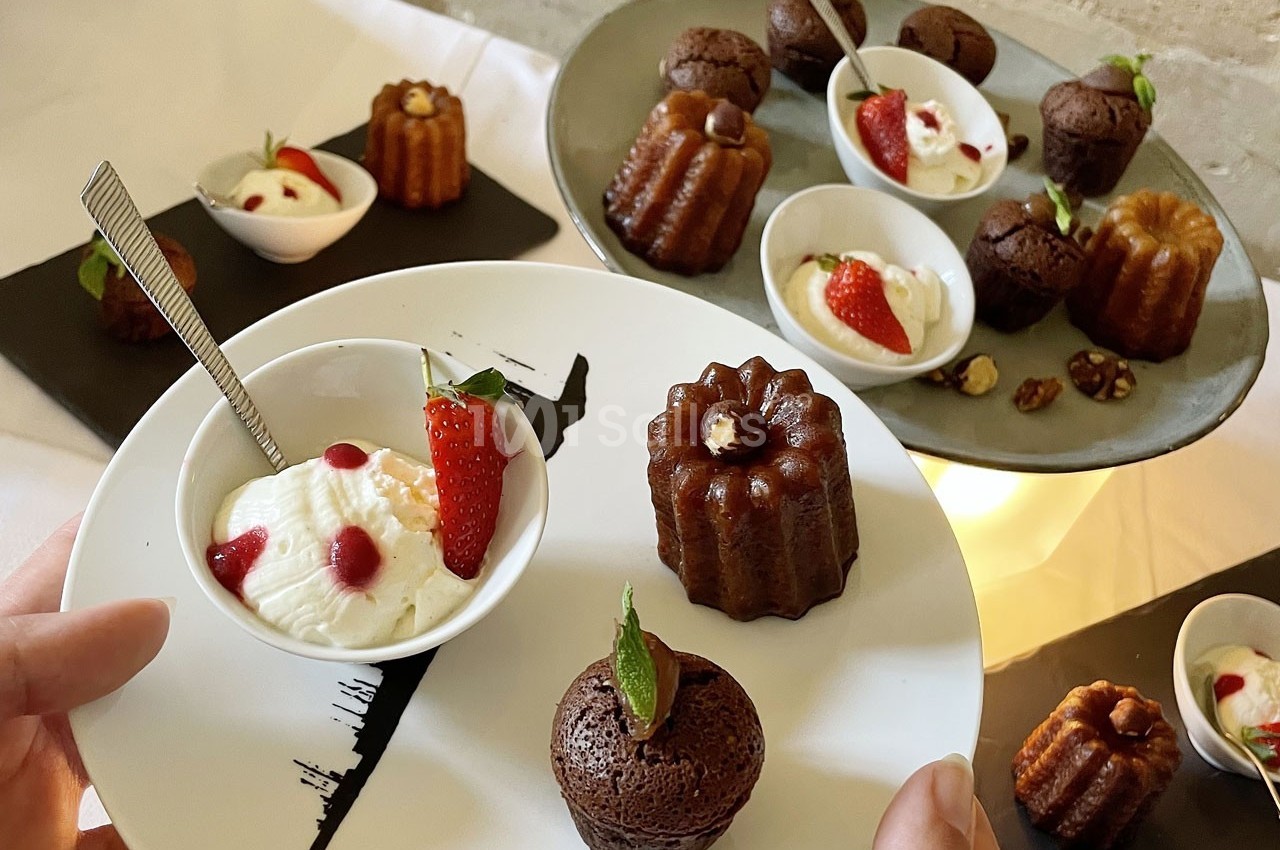 Assortiment de cannelés, moelleux au chocolat et verrines de crème décorées de fraises sur une table de dégustation.