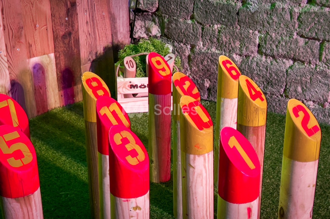 Quilles numérotées en bois coloré disposées sur une pelouse artificielle devant un mur en pierre.