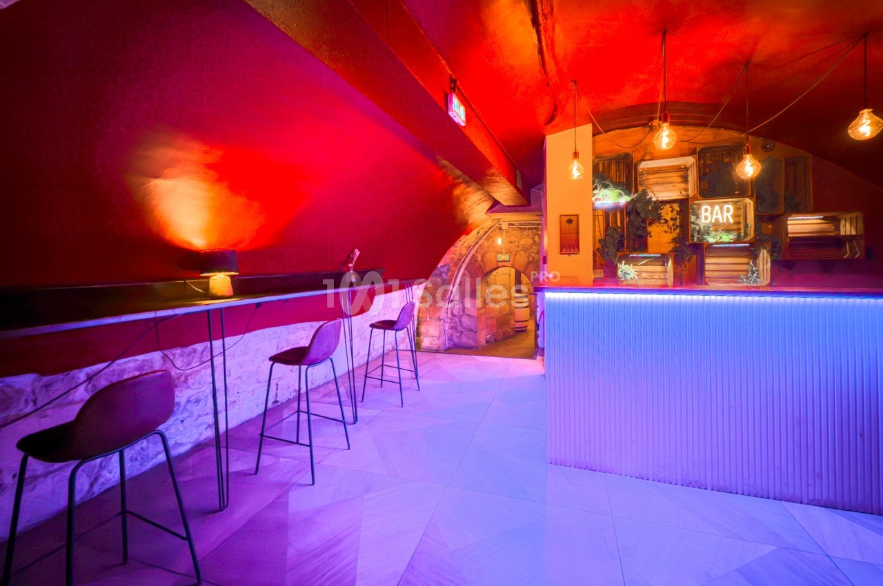 Intérieur d'un bar avec éclairage coloré, comptoir lumineux, chaises hautes et murs en pierre apparente.