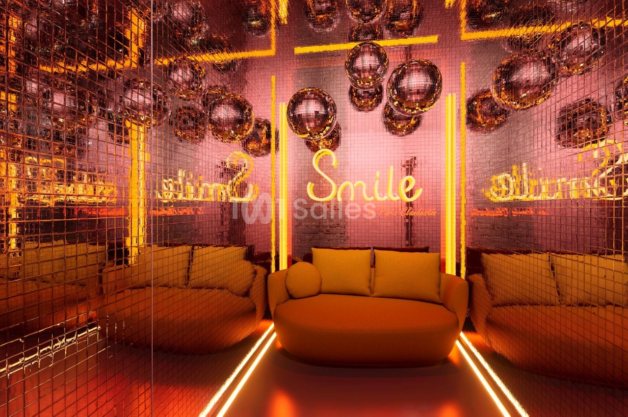 Salle aux murs recouverts de miroirs dorés, canapé orange et enseigne lumineuse ’Smile’ entourée de boules disco.