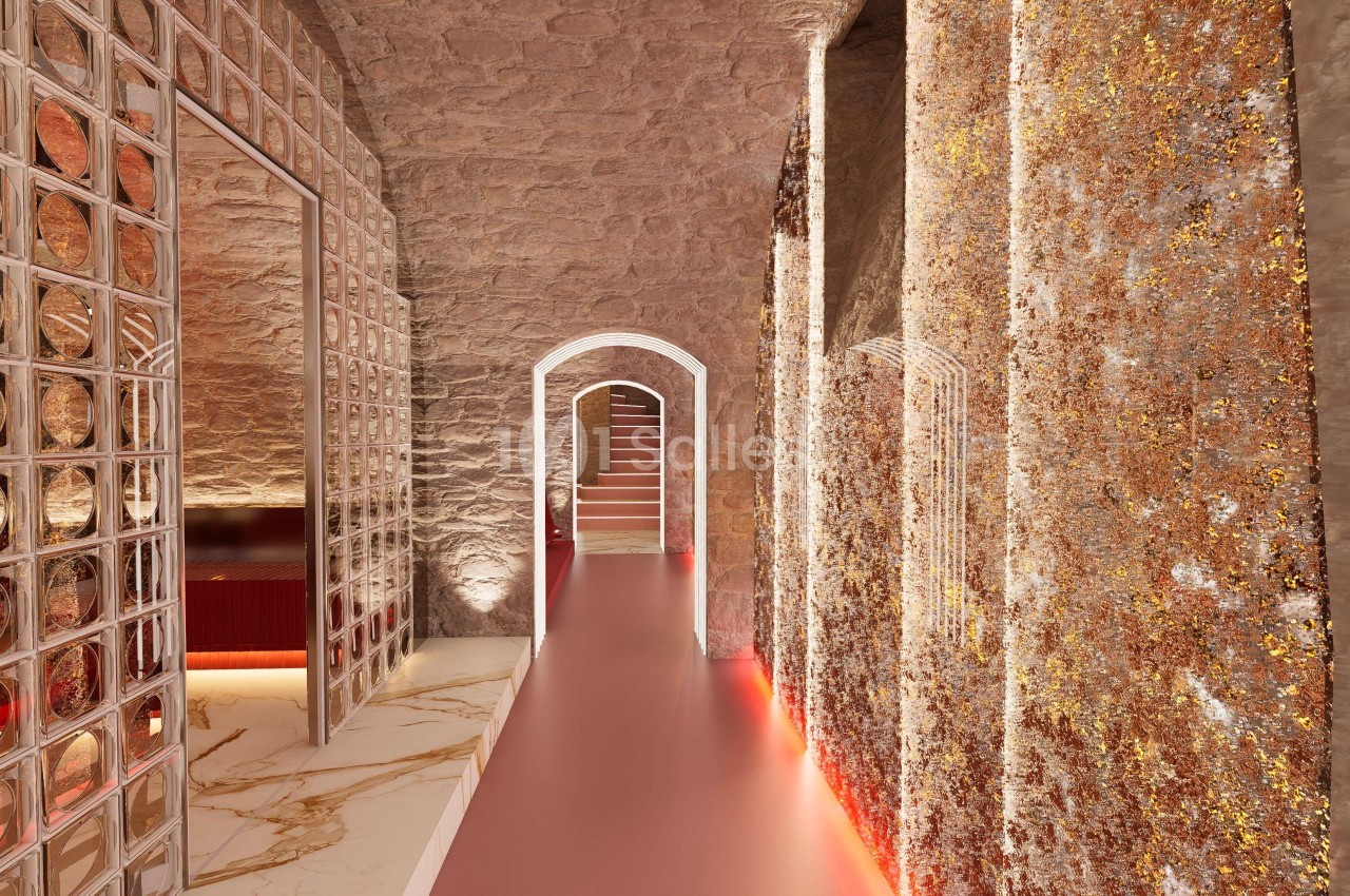 Couloir voûté avec murs texturés dorés, sol lisse et éclairage tamisé menant à un escalier en pierre.