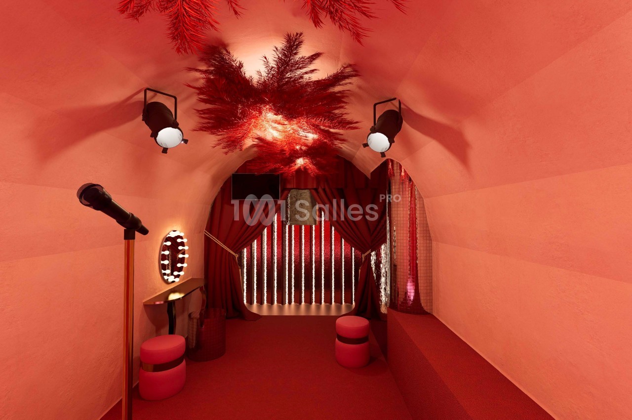 Salle immersive rouge avec rideaux, miroirs éclairés, tabourets et décorations suspendues en feuillage rouge.