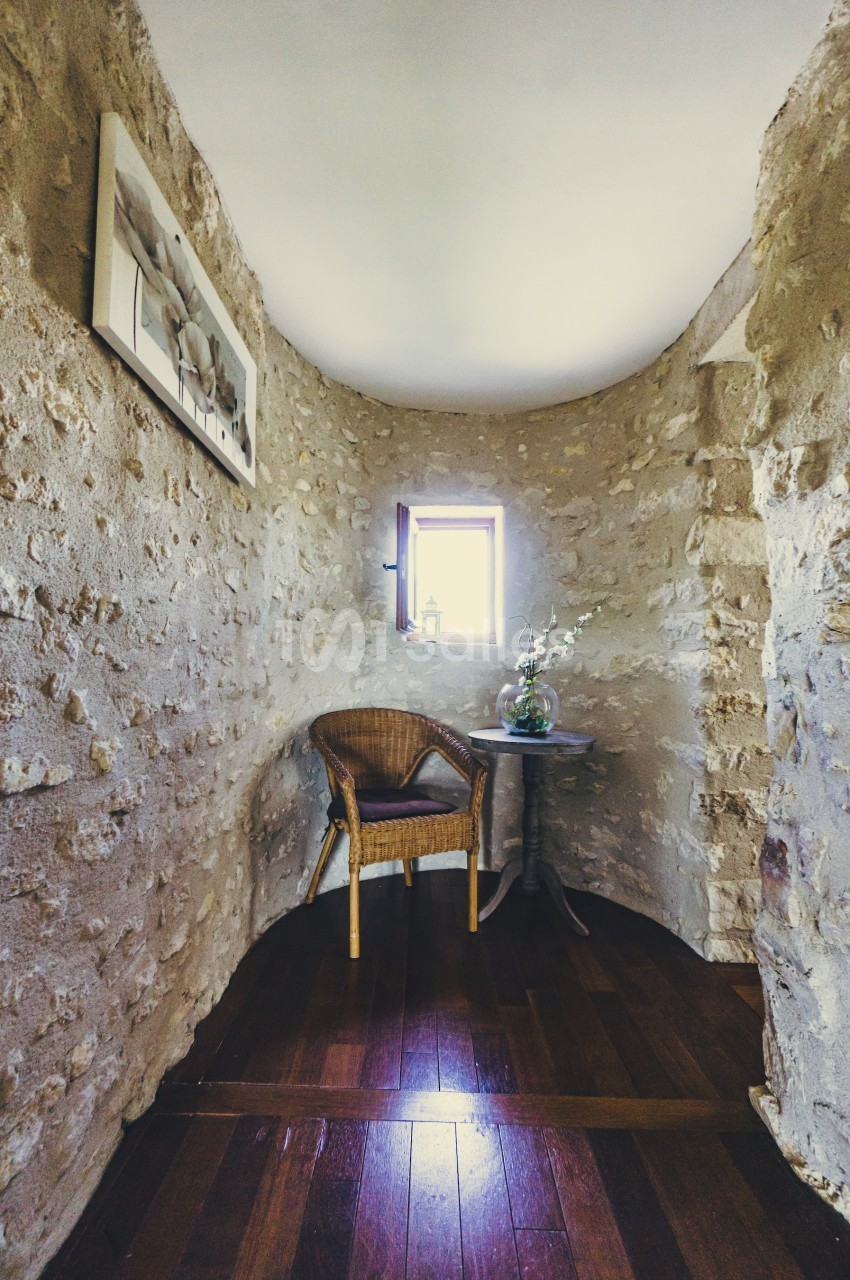 Coin d'une pièce en pierre avec une chaise en osier, une petite table ronde, un vase de fleurs et une fenêtre éclairant l…