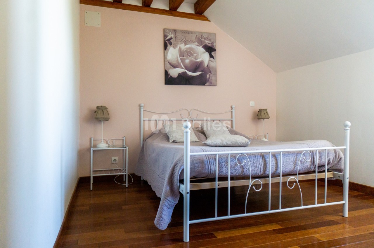 Chambre avec lit double en métal blanc, parquet en bois, murs clairs et tableau floral au-dessus du lit.