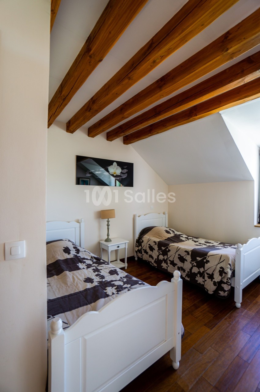 Deux lits simples avec couvre-lits à motifs floraux dans une chambre lumineuse avec poutres apparentes en bois.