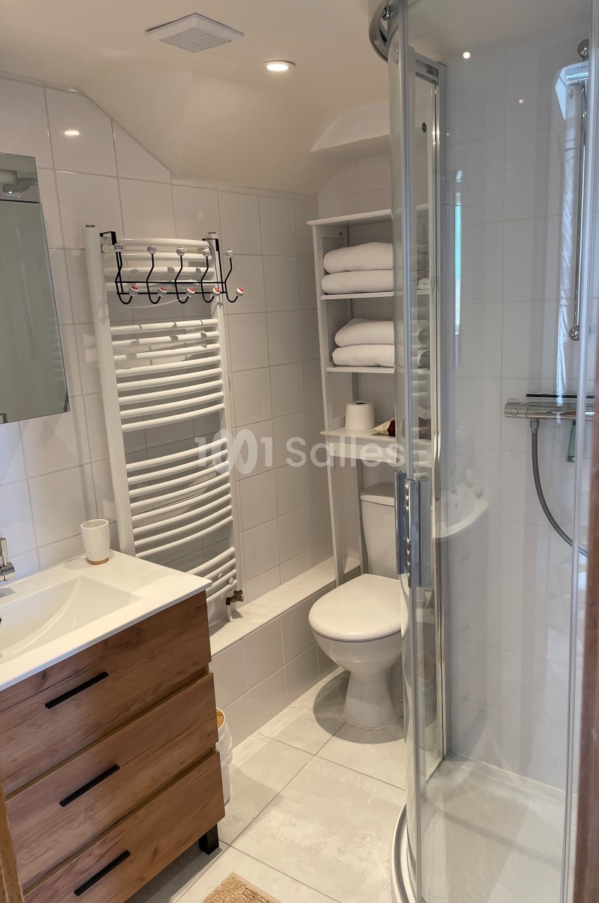 Salle de bain moderne avec douche arrondie, lavabo avec meuble en bois, toilettes et étagères avec serviettes.