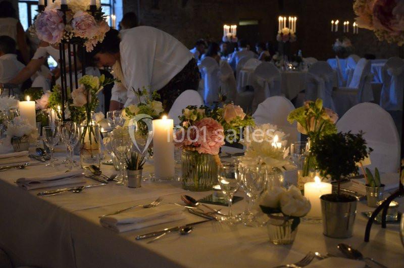 Table décorée pour un dîner élégant avec bougies, fleurs et vaisselle, dans une salle faiblement éclairée.
