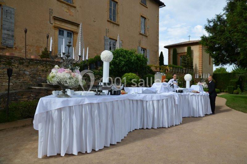 Buffet en plein air avec nappes blanches, installé devant un bâtiment ancien entouré de verdure.
