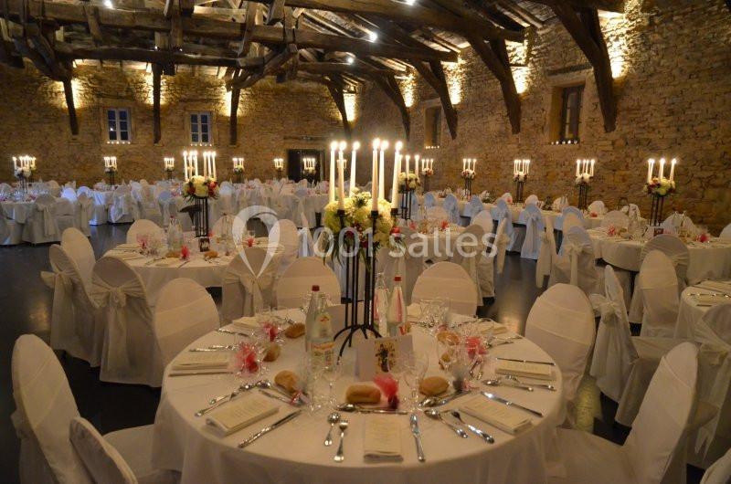 Salle en pierre avec des tables rondes décorées pour un événement, éclairée par des chandeliers et des lumières chaudes.