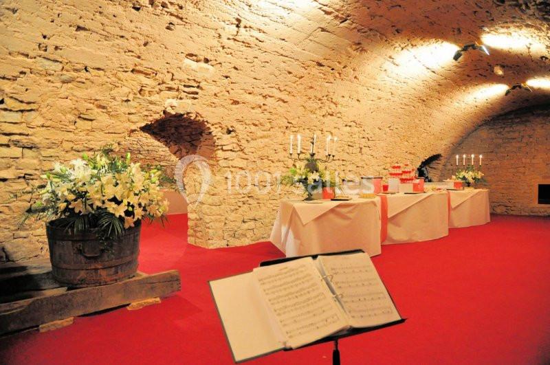 Salle voûtée en pierre avec nappes blanches, décorations florales et chandeliers, sur un sol recouvert de moquette rouge.