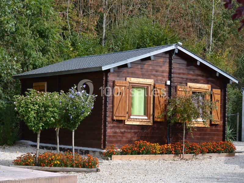 Chalet en bois entouré de fleurs et d'arbustes, situé dans un environnement arboré.
