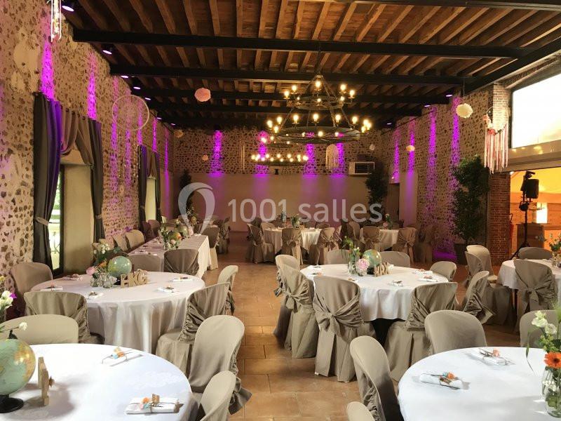 Salle de réception décorée avec des tables rondes, nappes beiges, chaises assorties et éclairage chaleureux.