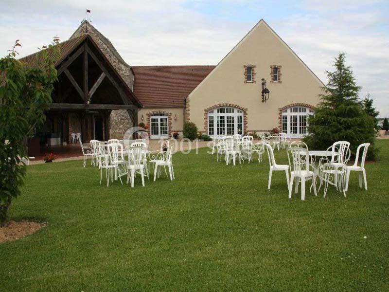 Chaises blanches disposées sur une pelouse devant un bâtiment en pierre et crépi avec toit en tuiles.